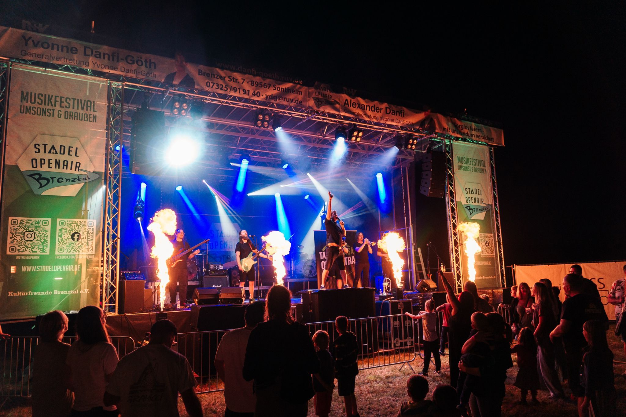 Festivalbühne bei Nacht mit Flammeneffekten, Bühnenlicht und Band vor Publikum