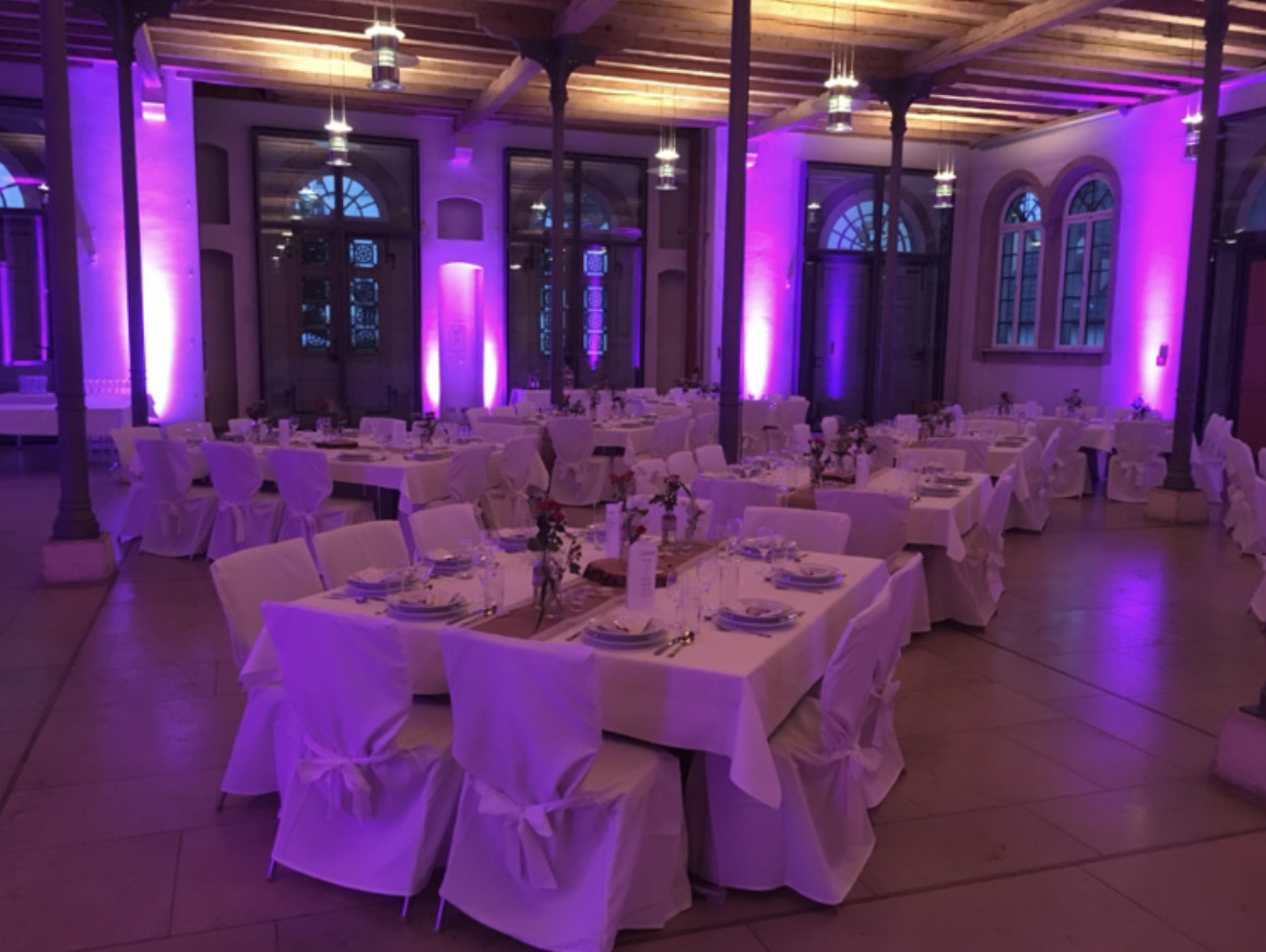Festlich gedeckter Hochzeitssaal mit weißen Stuhlhussen und dezenter violetter Ambientebeleuchtung
